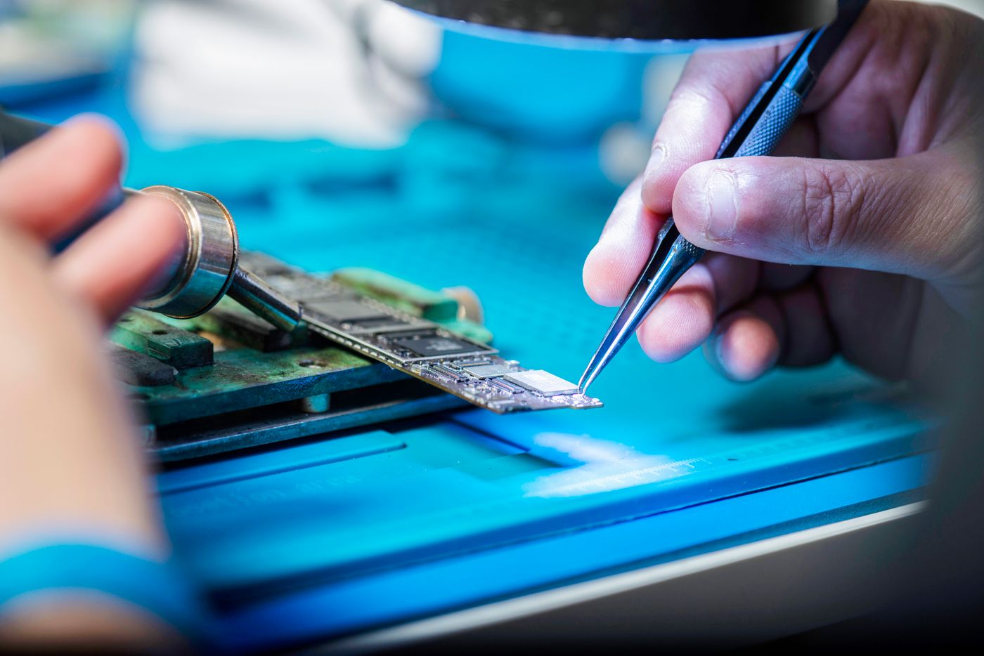 Hands carrying out detailed repair work on an electronic circuit board